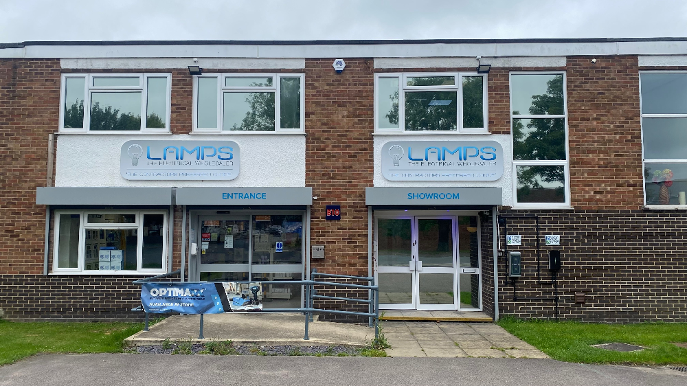 Photo of the LAMPS Bicester branch exterior showing the main entrance and showroom, with branded signage and EV chargers mounted on the front wall.